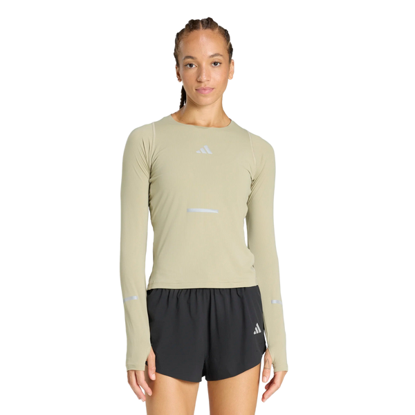 En person står og kigger fremad iført en Adidas Adi365 Long Sleeve Shirt i Dame Woca og sorte sportsshorts med et Adidas-logo på en almindelig hvid baggrund.