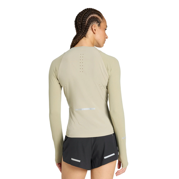 En kvinde med flettet hår ses bagfra i en tætsiddende beige Adidas Adi365 Long Sleeve Shirt, dame, woca, med små ventilationshuller, parret med sorte shorts med refleksstriber på en almindelig hvid baggrund.