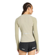 En kvinde med flettet hår ses bagfra i en tætsiddende beige Adidas Adi365 Long Sleeve Shirt, dame, woca, med små ventilationshuller, parret med sorte shorts med refleksstriber på en almindelig hvid baggrund.