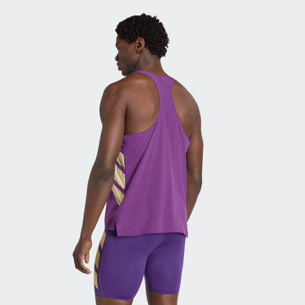 En mand står med ryggen til kameraet iført Adidas Rtr Singlet, Herre i violet - en atletisk tanktop med gule diagonale striber - og matchende lilla shorts med et lignende gult design. Baggrunden er almindelig og lys.