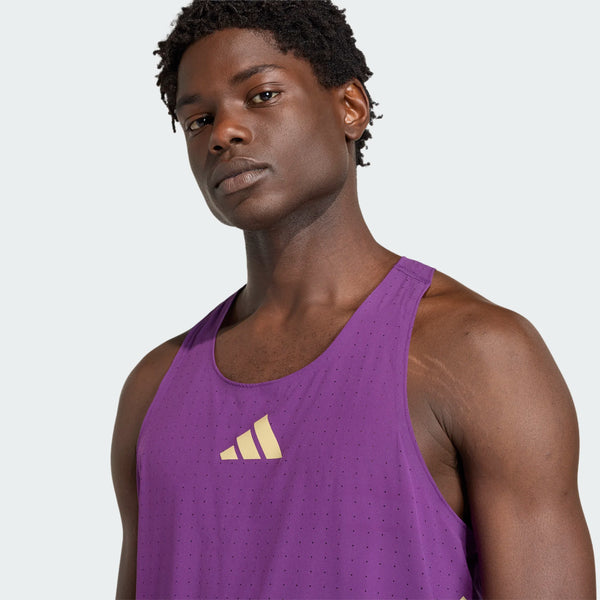 En person med kort krøllet hår bærer Adidas Rtr Singlet, Herre, i violet, med et gult logo på brystet, der står på en almindelig lysegrå baggrund.