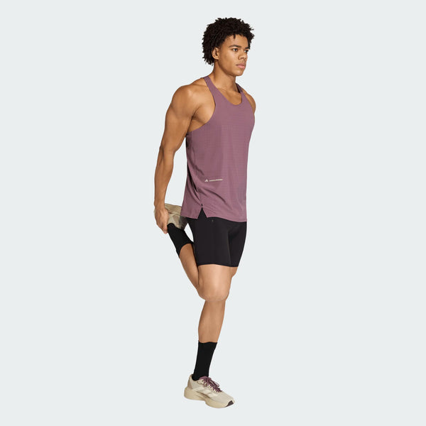 En mand iført Adidas Adi365 Hk Singlet i Shafig står og strækker sin højre quadriceps, mens han kombinerer singletten med sorte shorts, sorte sokker og lyse sneakers.