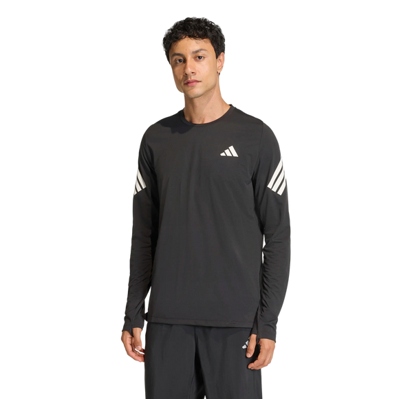 En mand står på en almindelig hvid baggrund iført Adidas Adi365 langærmet skjorte til mænd i sort med tre hvide striber på hvert ærme og et lille hvidt logo på brystet, sammen med matchende sorte bukser.