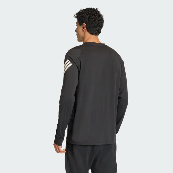 En mand med kort krøllet hår ses bagfra iført Adidas Adi365 Long Sleeve Shirt, Herre, i sort med tre hvide striber på højre skulder og matchende sorte bukser på en lysegrå baggrund.