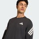 En mand i Adidas Adi365 Long Sleeve Shirt, Herre, Black, med et hvidt geometrisk brystlogo og tre hvide striber på hvert ærme, kigger lidt til siden mod en ensfarvet baggrund.