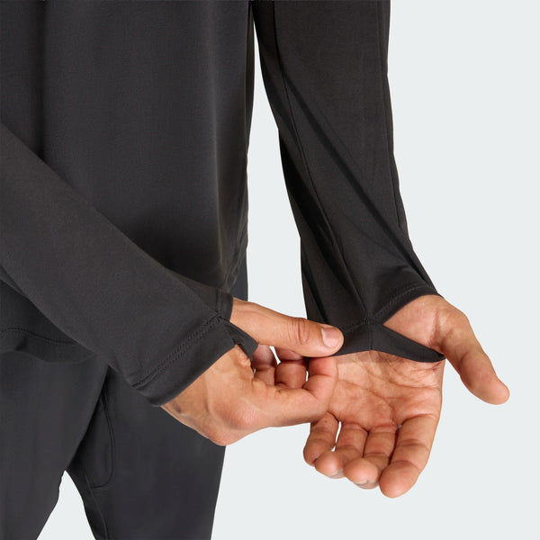 En person iført Adidas Adi365 Long Sleeve Shirt, Herre, Black demonstrerer tommelfingerhullet ved at trække manchetten over hånden og vise, hvordan tommelfingeren passer gennem åbningen.