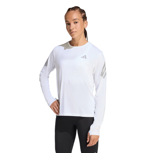 En kvinde ser fremad iført Adidas Adi365 langærmet skjorte i hvid med diskrete logodetaljer på brystet og ærmerne, sammen med sorte leggings på en almindelig hvid baggrund.