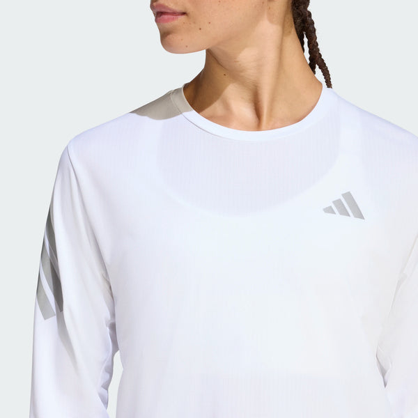 En kvinde er iført Adidas Adi365 Long Sleeve Shirt i hvid med Adidas-logo på brystet og skulderstriber, fotograferet fra skuldrene og op mod en ensfarvet baggrund.