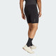En person iført Adidas Adi365 Hk Tight shorts i sort står med ryggen til kameraet, parret med en mørk t-shirt, sorte strømper og hvide sportssko mod en almindelig lys baggrund.