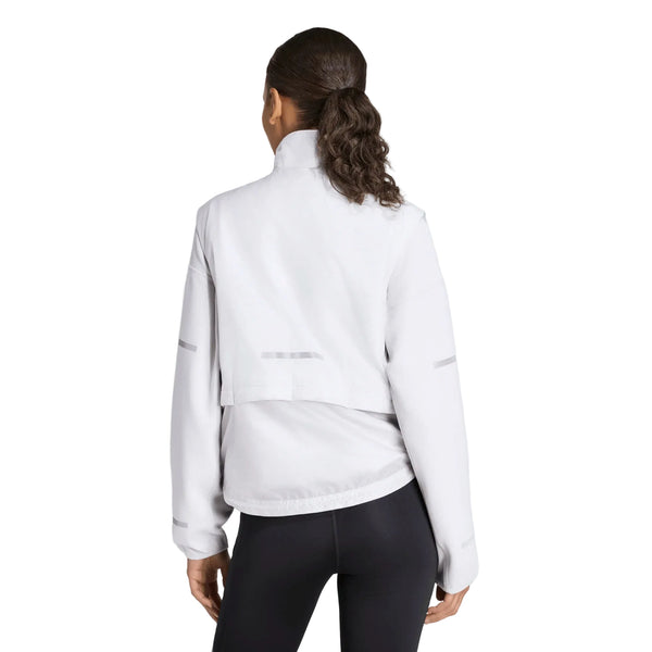 Der ses et billede bagfra af en person med mørkt hår i hestehale, iført en lysegrå Adi365 Running Warm Vest til kvinder fra Adidas og sorte leggings, stående foran en ensfarvet hvid baggrund.