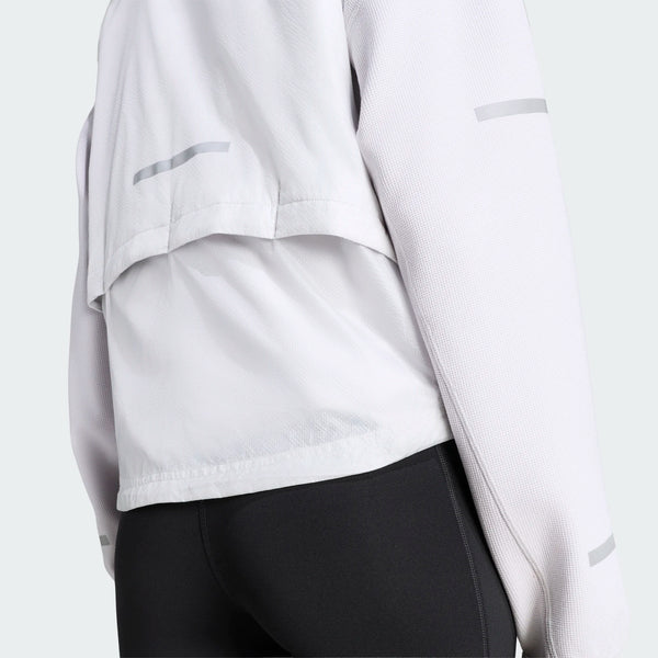 En person iført Adidas Adi365 Running Warm Vest til kvinder i grøn, som er udstyret med refleksstriber og en ventilationsklap øverst på ryggen for bedre åndbarhed. Den vandafvisende vest ses her set bagfra og er kombineret med sorte leggings, der slutter ved taljen.