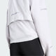En person iført Adidas Adi365 Running Warm Vest til kvinder i grøn, som er udstyret med refleksstriber og en ventilationsklap øverst på ryggen for bedre åndbarhed. Den vandafvisende vest ses her set bagfra og er kombineret med sorte leggings, der slutter ved taljen.