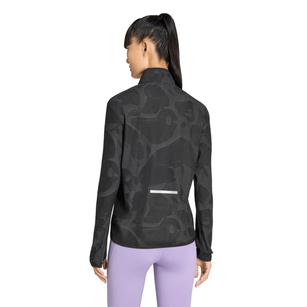 En kvinde med hestehale står med ryggen til kameraet iført lavendelblå leggings og en Adidas Adi365 Running Half Zip-jakke i farven Black/Grefiv. Jakken er designet til kvinder med climawarm+-teknologi og har en diskret refleksstribe nederst på ryggen.