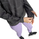 En kvinde ses iført en Adidas Adi365 Running Half Zip i farven Black/Grefiv, der har et mønstret design med lange ærmer og tommelfingerhuller. Hun har den på sammen med lyselilla leggings og sorte sportssko. Hendes ansigt kan ikke ses, da hun med højre hånd retter på trøjen med halv lynlås, hvilket fremhæver dens funktionelle design.
