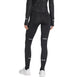 En person står med ryggen til kameraet og er iført en sort langærmet bluse, hvide sneakers og et par sorte Adidas Adi365 Climawarm+ løbetights til kvinder med diskrete refleksstriber. Baggrunden er ensfarvet hvid.