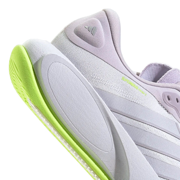 Nærbillede af adidas Supernova Prima 3 Dame-løbeskoen i farvekombinationen Fropur/Whitin/Hireye, der fremhæver det lyselilla og hvide design med neongrønne detaljer på sålen. Den strukturerede ydersål giver forbedret greb, mens tre diagonale striber pryder siden, og et lille præget trekantlogo ses på hælen.