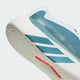Nærbillede af siden og sålen på et par blågrønne og hvide Adidas Hyperboost Edge herreløbesko (Ftwwht/Petmet/Lucred), med en struktureret hvid sål, blågrøn overdel med hvide diagonale striber og et lille rødt mærke på undersiden – hvilket understreger det enestående komfortfokuserede design til vejløb fra Adidas.