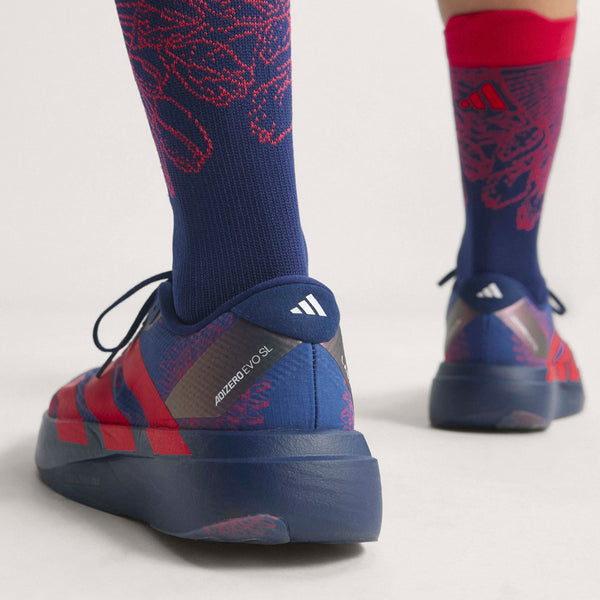 En person iført Adidas Adizero Evo SL Woven herre i dkblue/lucred/mutprp med matchende mønstrede sokker, fotograferet bagfra i ankelhøjde. Adidas-logoet og ADIZERO SL er synlige og fremhæver den avancerede LIGHTSTRIKEPRO-støddæmpning.