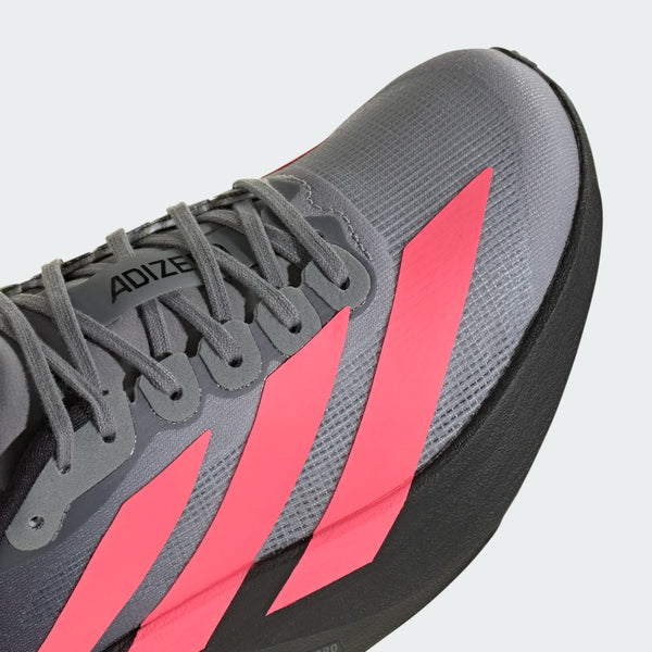 Nærbillede af Adidas Adizero Evo SL Dame-løbeskoen i farvekombinationen Cblack/Soltur/Ltonix, med lyserøde diagonale striber, grå snørebånd og en tyk sort sål. Denne løbesko er fremstillet af åndbart, letvægtsmateriale med »ADIZERO« på tungen og er udstyret med responsivt LIGHTSTRIKE PRO-skum, der sikrer optimal komfort og hastighed på hver eneste løbetur.