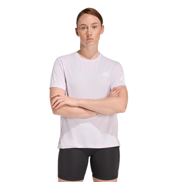 En kvinde med kort brunt hår iført Adidas Adi365 Running Tee, Dame, Icelav og sorte shorts står med armene over kors på en almindelig hvid baggrund.