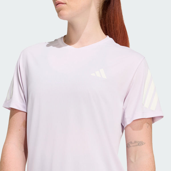 En person med langt rødt hår er iført en Adidas Adi365 Running Tee, Dame, Icelav, med hvide diagonale ærmestriber og et lille logo på brystet. En biltatovering er synlig på højre underarm.