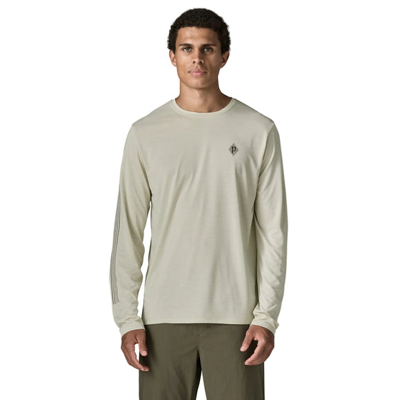 En mand står med ansigtet vendt fremad og har en lysbeige Patagonia L/S Cap Cool Daily Shirt – Hut Tripper, Herre, Dyno White – fremstillet af genbrugt polyester – samt olivengrønne bukser på. Hans arme hviler langs siden, og han har kort, krøllet hår. Baggrunden er ensfarvet hvid.