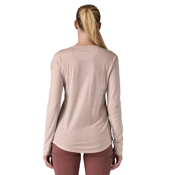 En kvinde med langt blondt hår i hestehale ses bagfra iført Patagonia W's L/S Cap Cool Merino Blend Graphic Shirt i Fitz Roy Strata/Shroom Taupe og lilla bukser på en almindelig hvid baggrund.