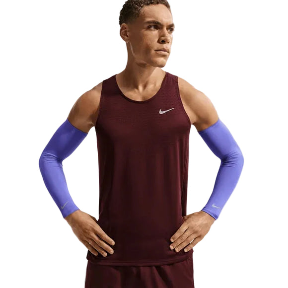 En mand i en rødbrun ærmeløs Nike-top, matchende shorts og blå Nike Lightweight Sleeves 2.0 (unisex) står med hænderne på hofterne og kigger lidt til siden.