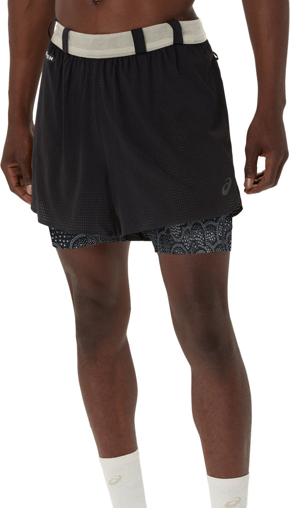 En person er iført ASICS Limited Series Metarun 4In 2-N-1 Shorts, Herre, i Performance Black/Cream med lyse mønstrede kompressionsshorts indenunder og hvide sokker. Shortsene har en elastisk linning og et lille logo på venstre ben.