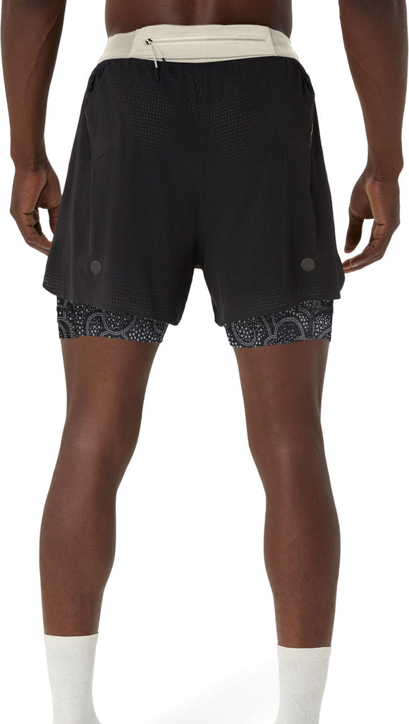 En person ses bagfra iført ASICS Limited Series Metarun 4In 2-N-1 Shorts til mænd i Performance Black/Cream, med en let linning og mønstrede kompressionsshorts indenunder, med hvide sokker mod en almindelig hvid baggrund.