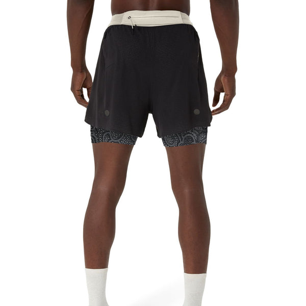 En person ses bagfra iført ASICS Limited Series Metarun 4In 2-N-1 Shorts til mænd i Performance Black/Cream, med en let linning og mønstrede kompressionsshorts indenunder, med hvide sokker mod en almindelig hvid baggrund.