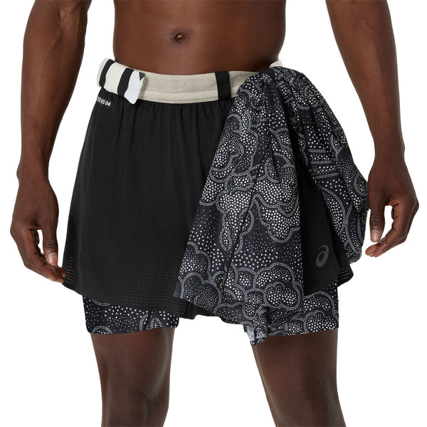 En person iført Asics Limited Series Metarun 4In 2-N-1 Short i Performance Black/Cream med et mønstret sort/hvidt håndklæde draperet over linningen. Kun overkroppen og overbenene er synlige.