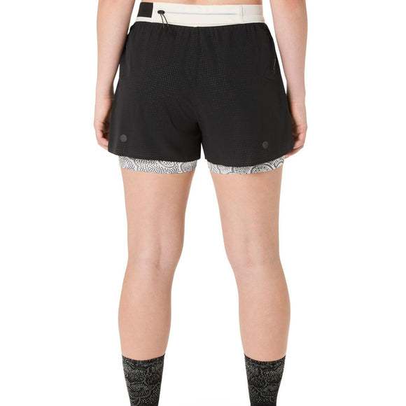 En person ses bagfra iført ASICS Limited Series Metarun Split Short til kvinder i Performance Black med hvid linning og mønstret inderfor; kun den nederste del af ryggen og benene er synlige.