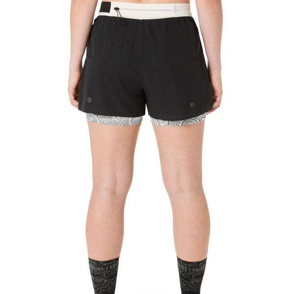 En person ses bagfra iført ASICS Limited Series Metarun Split Short til kvinder i Performance Black med hvid linning og mønstret inderfor; kun den nederste del af ryggen og benene er synlige.