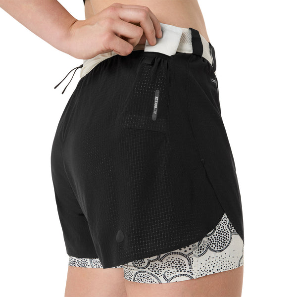 En kvinde er iført sorte Asics Limited Series Metarun Split Shorts med hvid linning, mønstret for og justerer linningslommen. Shortsene har en baglomme med lynlås og et lille Asics-logo på siden.