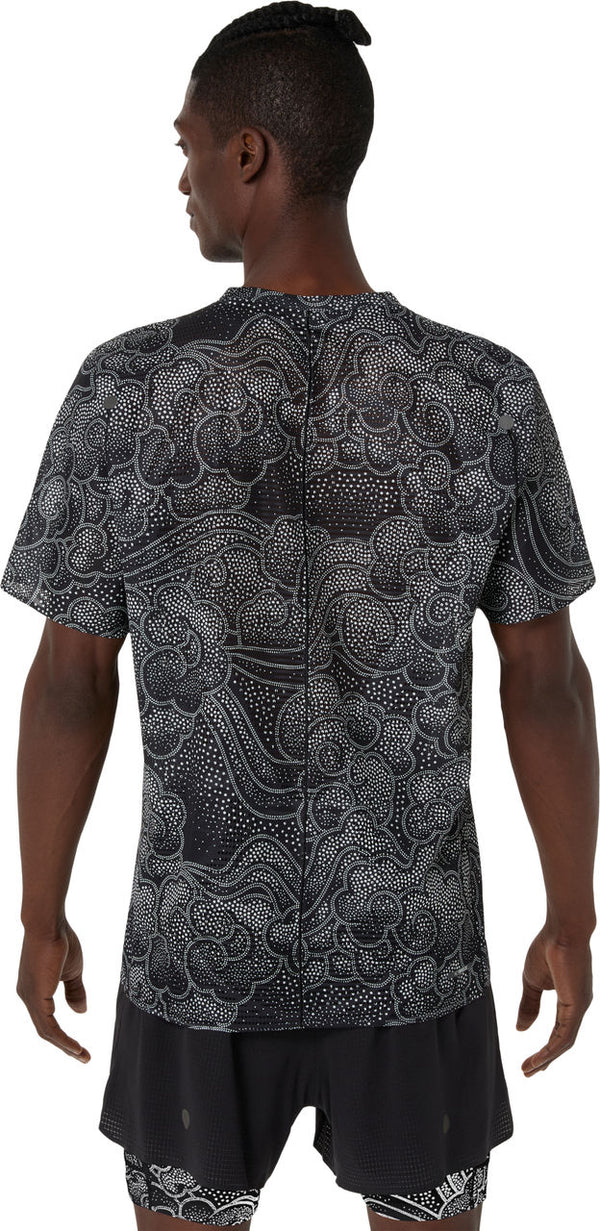 En person med topknude ses bagfra i Asics Limited Series Metarun SS Top, Herre, Performance Black og sorte shorts - ideel til løbetræning takket være ACTIBREEZE-teknologi og et hvidt abstrakt prikket mønster.