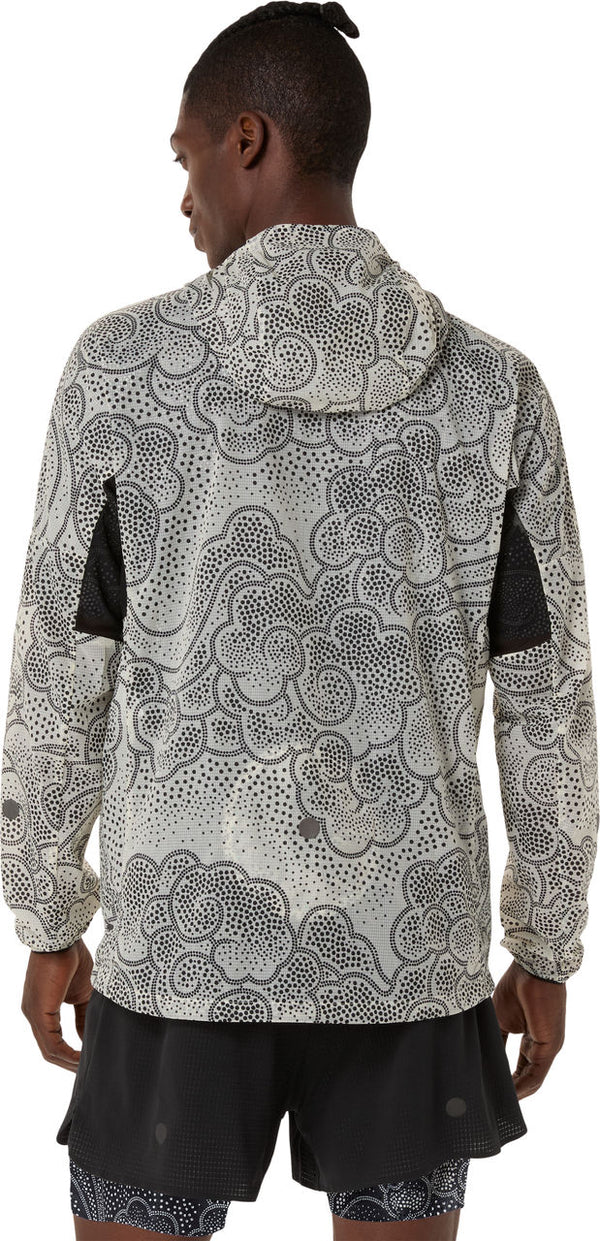 En person står med ryggen til og er iført en ASICS Limited Series Wind Breaker Jacket, Herre, Performance Black/Cream med et sort abstrakt prik- og hvirvelmønster, sorte mesh-albuepaneler og sorte shorts.