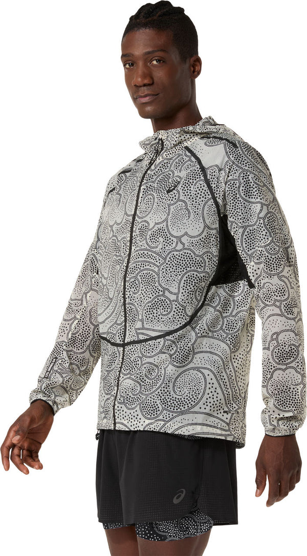 En person i en ASICS Limited Series Wind Breaker Jacket, Herre, Performance Black/Cream står vinklet til siden, iført sorte løbeshorts og kigger ind i kameraet.