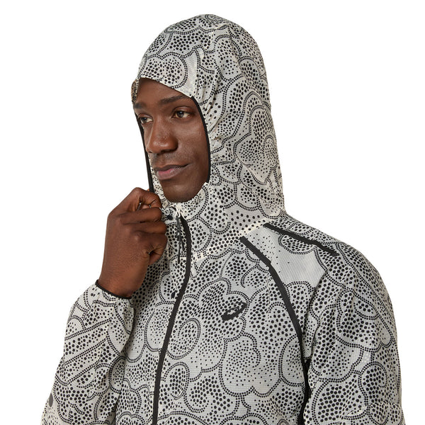 En person iført ASICS Limited Series Wind Breaker Jacket, Herre, i Performance Black/Cream med hætten oppe lyner den og kigger til siden.