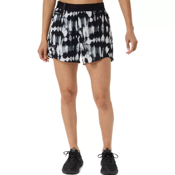 En person har Asics Limited Series Metarun Split Shorts til kvinder i farven Cream/Performance Black på, med sort linning, og er iført sorte sportssko. Billedet viser personen fra midten af overkroppen og ned til fødderne foran en ensfarvet baggrund.
