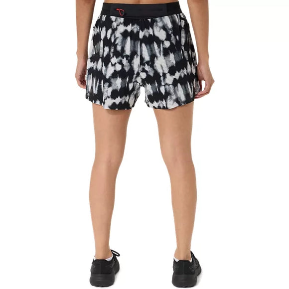 En person står med ryggen til, iført sorte sneakers og ASICS Limited Series Metarun Split Shorts til kvinder i farvekombinationen Cream/Performance Black – et stilfuldt par løbeshorts til kvinder med et sort-hvidt tie-dye-mønster og en kontrastfarvet sort linning. Hænderne hviler ned langs siden på en ensfarvet hvid baggrund.