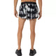 Der ses en person set bagfra, iført ASICS Limited Series Metarun Split Shorts til mænd i farvekombinationen Cream/Performance Black, sammen med sorte sko og uden trøje, stående foran en ensfarvet hvid baggrund.
