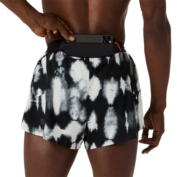 En person, der bærer et par Asics Limited Series Metarun Split Shorts, Herre, i farven Cream/Performance Black fra ASICS Limited Series, stikker en smartphone ned i en lomme bag på linningen, mens hånden hviler på telefonen, og den bare overkrop er delvist synlig.