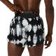 En person, der bærer et par Asics Limited Series Metarun Split Shorts, Herre, i farven Cream/Performance Black fra ASICS Limited Series, stikker en smartphone ned i en lomme bag på linningen, mens hånden hviler på telefonen, og den bare overkrop er delvist synlig.