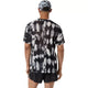En person står med ryggen til og har en Asics Limited Series Metarun Ss Top til mænd i farven Cream/Performance Black på – en teknisk løbetrøje med løs pasform og korte ærmer – kombineret med sorte shorts og en mønstret kasket. Baggrunden er ensfarvet og overskuelig.