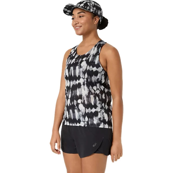 En kvinde står og smiler iført ASICS Limited Series Metarun Tank til kvinder i farvekombinationen Cream/Performance Black med ACTIBREEZE-teknologi, kombineret med sorte sportsshorts og en matchende mønstret kasket. Hun vender sig let mod venstre foran en hvid baggrund.