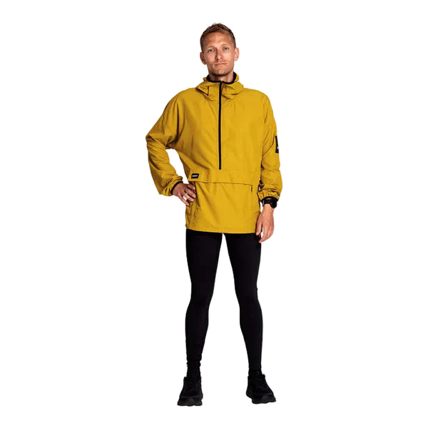 En person iført sennepsgul jakke med hætte, sorte Saysky Logo Motion+ Long Tights, Herre og sorte sko står med front mod en hvid baggrund med den ene hånd på hoften.