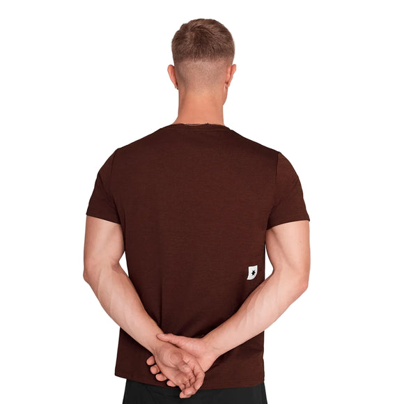 En mand med kort hår står med ryggen til og har en tætsiddende rød Saysky Logo Pace-T-shirt til mænd og sorte bukser på. Han har begge hænder foldet bag ryggen, og der kan ses et lille hvidt mærke nederst på trænings-T-shirten.