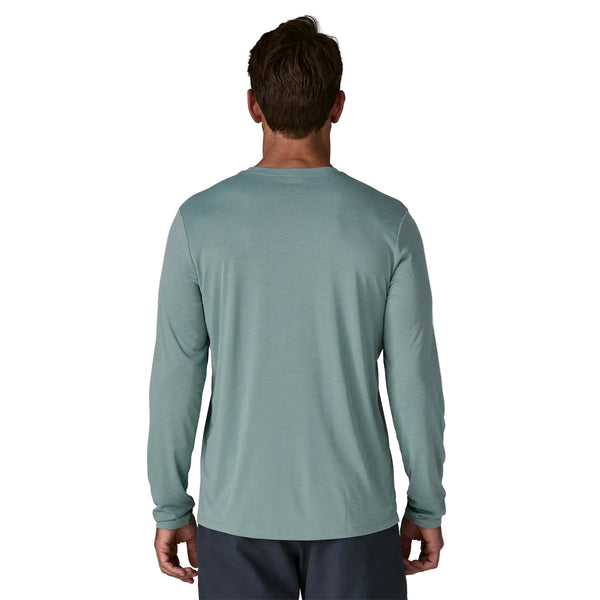 En person kigger væk fra kameraet iført en Patagonia Long-Sleeved Capilene Cool Shirt til mænd i Blue Sage - Light Blue Sage X-Dye og mørke shorts på en almindelig hvid baggrund.