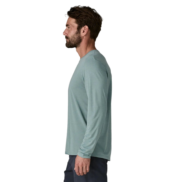 En mand med brunt hår og skæg ses i profil, iført en Patagonia Long-Sleeved Capilene Cool Shirt for men i Blue Sage - Light Blue Sage X-Dye, sammen med mørke bukser, stående mod en hvid baggrund.